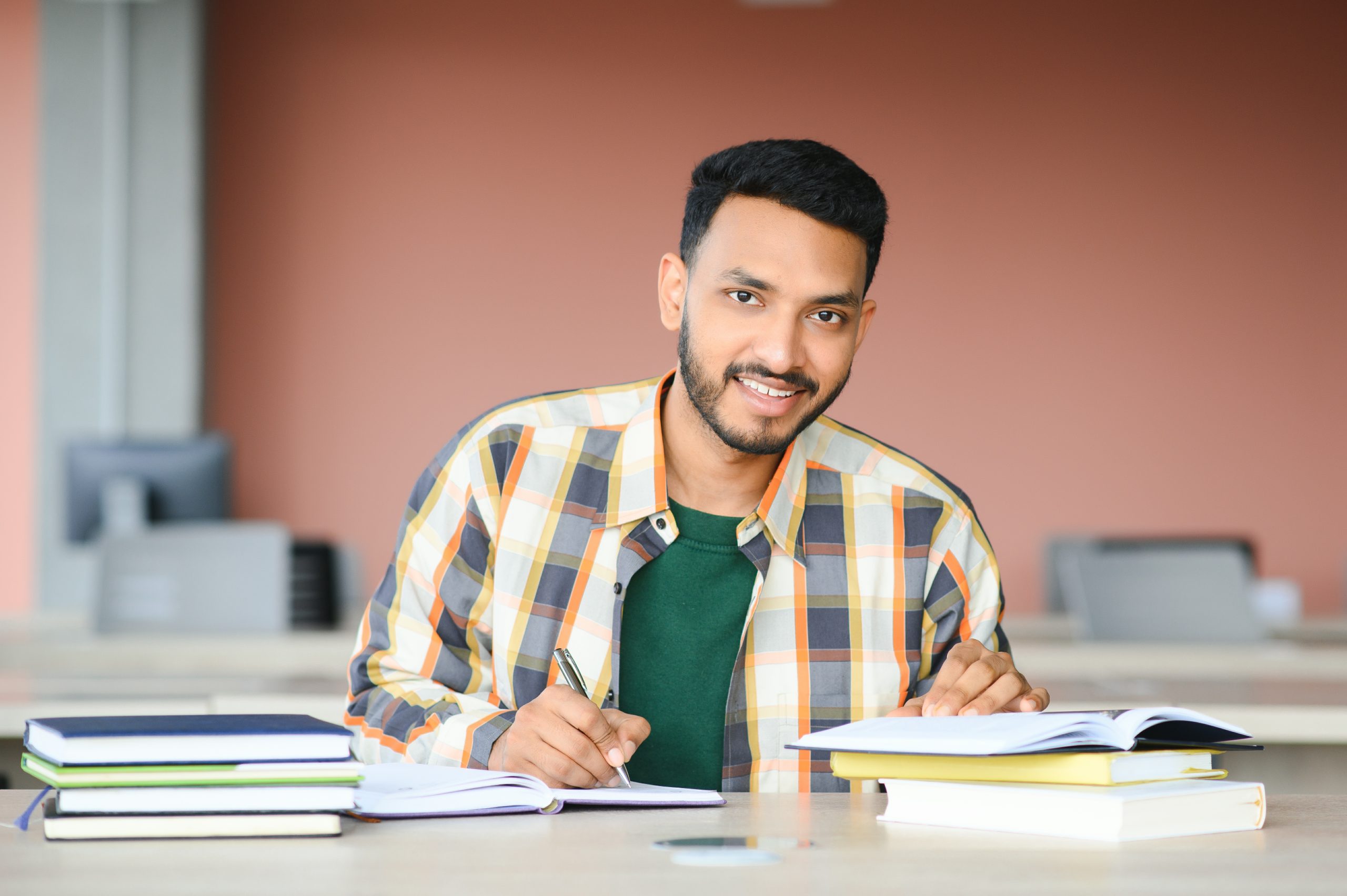 Smiling student writing in a notebook surrounded by stacked books, reflecting the confidence and strong study habits built through Tutor of Dragons' personalized SAT/ACT test prep tutoring.