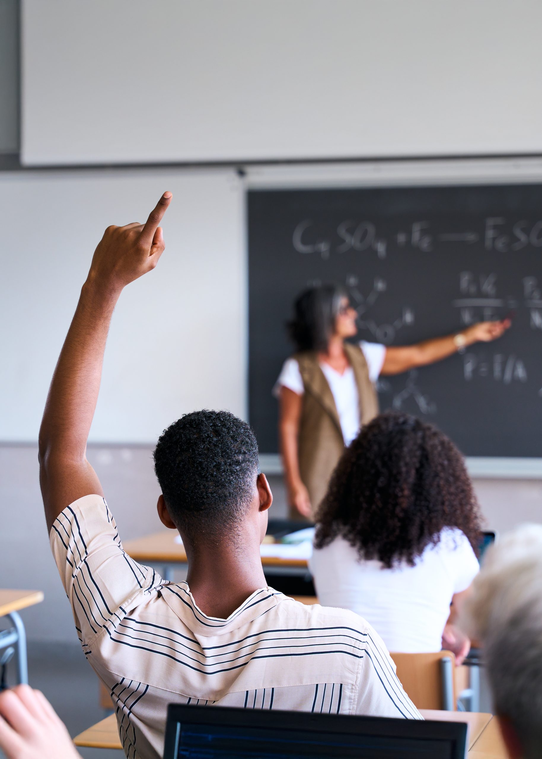 Student raising a hand to ask a question while an instructor explains equations at a chalkboard in an AP Pre-Calculus tutoring session with Tutor of Dragons in Southlake, Texas